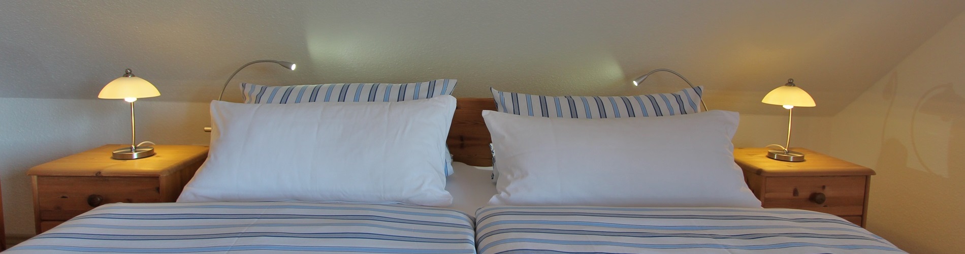 Bettteil mit bezogenen Kopfkissen, Nachtischlampen und Leselampen der Fereinwohnung Talblick